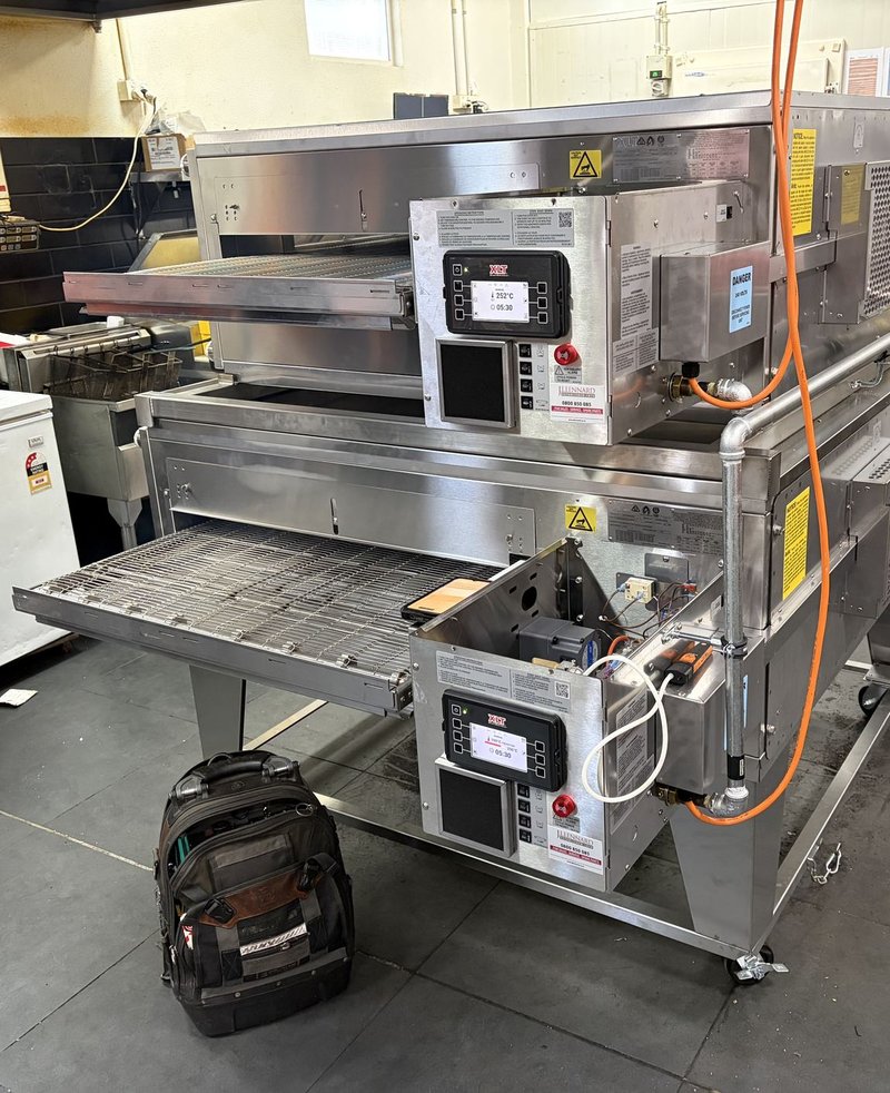 New stacked XLT conveyor ovens mid-install, with the control panel open and gas and electrical connections in place