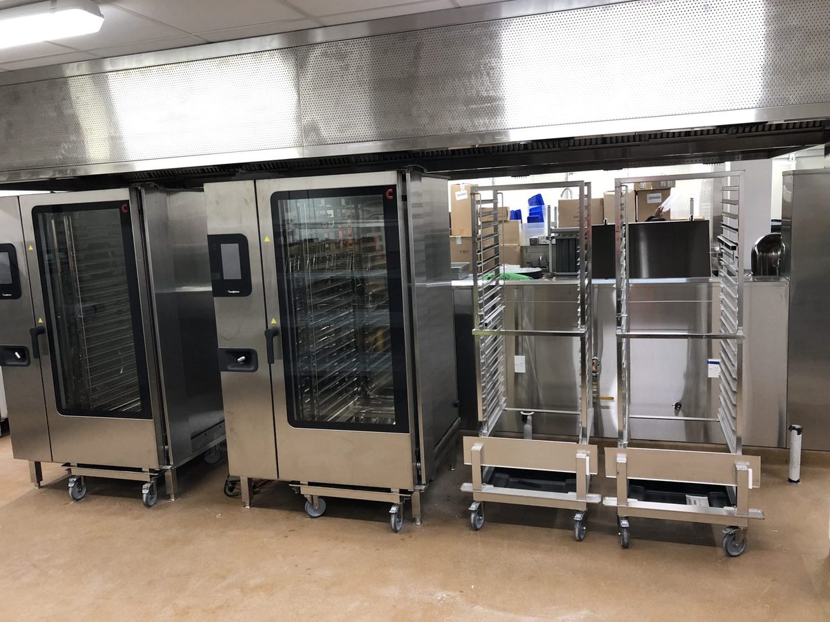 Two roll-in commercial combi ovens with mobile tray trolleys in a commercial kitchen