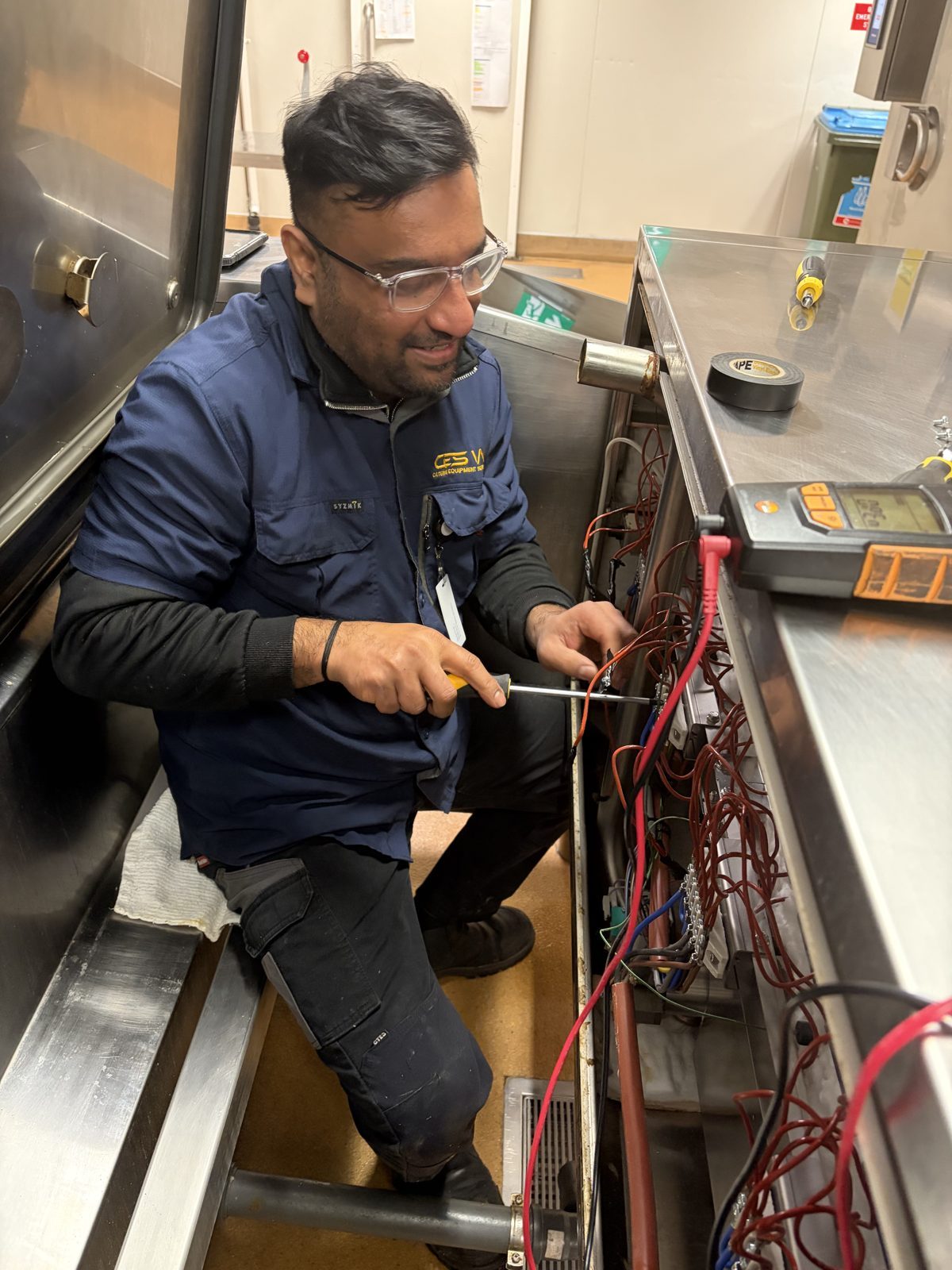 Registered technician testing the electrical wiring of a commercial kitchen appliance with a multimeter