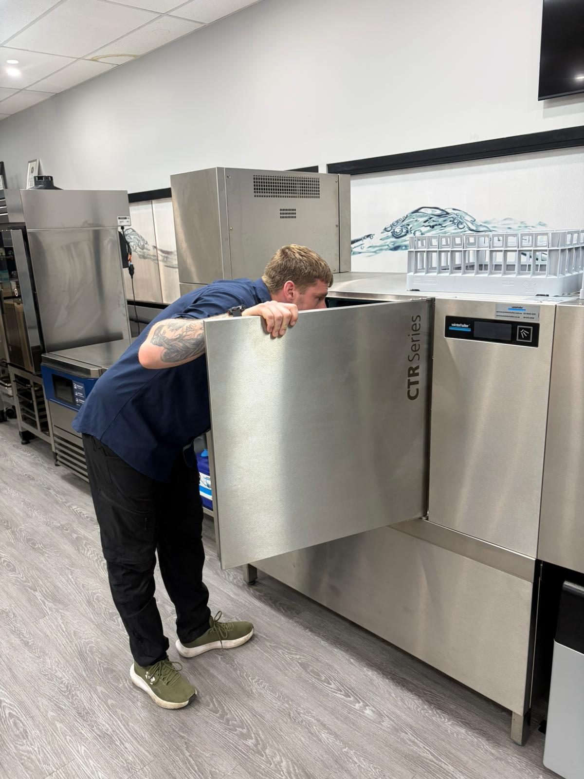Technician inspecting the inside of a Winterhalter CTR Series rack conveyor dishwasher